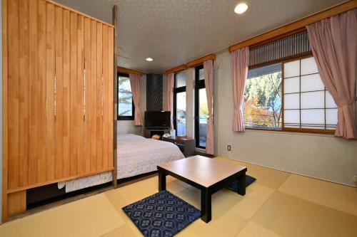 a bedroom with a bed and a table and windows at 栂池高原　丘の上ホテル in Otari