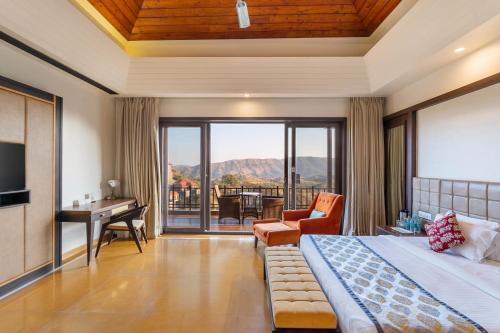 a bedroom with a bed and a desk and a balcony at Mahua Bagh Resort Kumbhalgarh in Kumbhalgarh