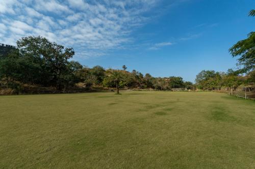 a large grass field with trees in the background at Mahua Bagh Resort Kumbhalgarh in Kumbhalgarh