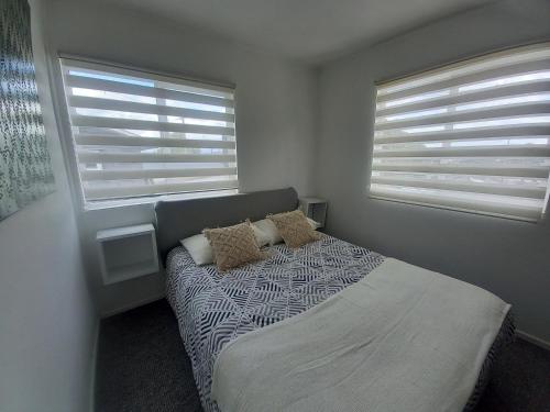 a bedroom with a bed and two windows at Cabañas Cerca del Centro in Puerto Montt