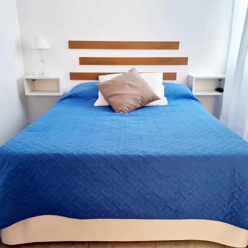 a bed with a blue comforter and a pillow at Dpto MARINE in Caleta Olivia