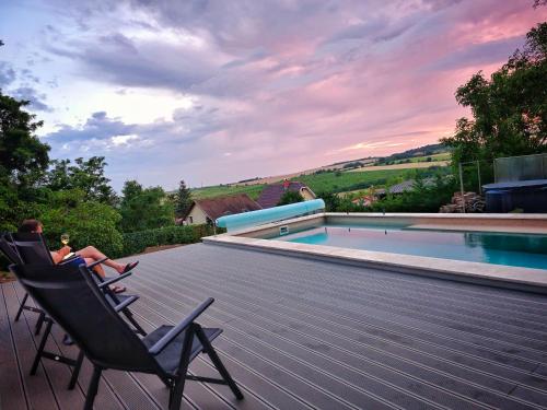 a man sitting in chairs on a deck next to a swimming pool at Tiétek a HÁZ in Mogyoród