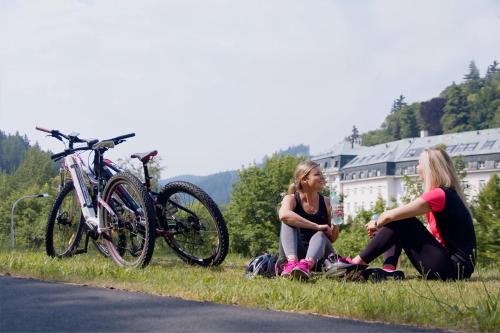 two women sitting on the grass next to a bike at Hotel Astoria in Jáchymov