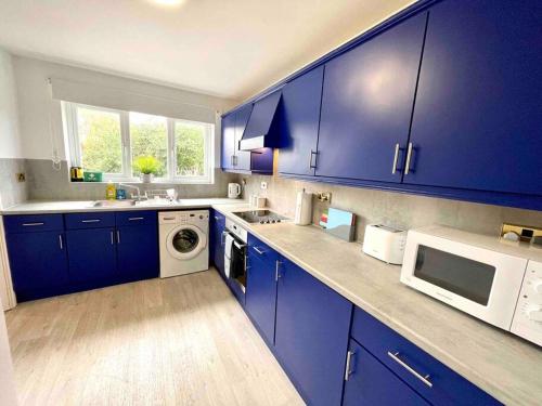 La cuisine est équipée de placards bleus et d'un four micro-ondes blanc. dans l'établissement Large 5 bed detached house near Stansted Airport, à Stansted Mountfitchet