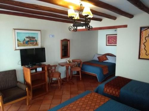 a room with two beds and a tv and a table at Hotel Villa Cristina in Villa de Leyva