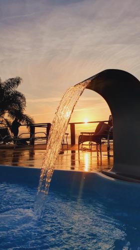 una fuente de agua en una piscina con la puesta de sol en el fondo en Pousada Vila de Monaco, en Penha