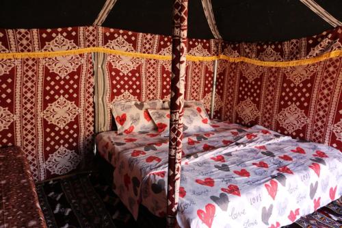 a bedroom with a bed with a red and white comforter at Desert Private Camps - Private Bedouin Tent in Shāhiq