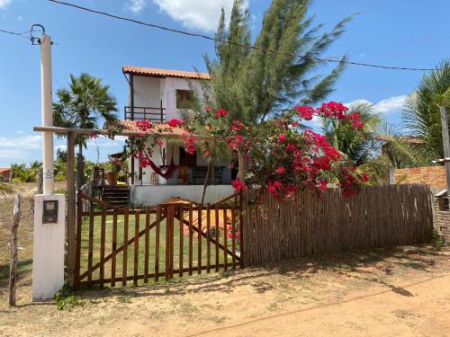 ein Haus hinter einem Zaun mit roten Blumen in der Unterkunft Chalé na Praia de Macapá Piaui in Luis Correia