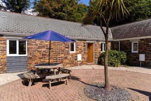 a picnic table with a blue umbrella next to a building at Trewhiddle 41 by Together Travel - Stylish Coastal Countryside Retreat in St Austell