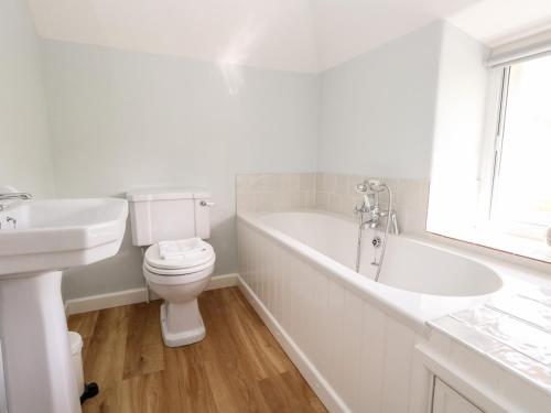 a white bathroom with a tub and a toilet and a sink at Dairy Cottage in Weymouth