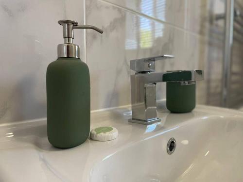 un distributeur de savon vert assis sur un lavabo dans la salle de bains dans l'établissement Ramson's Homestead by M-GroupSA, à Cardiff