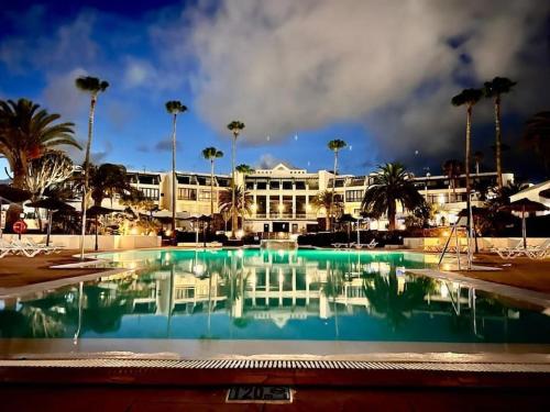 a large pool in front of a building with palm trees at RockBeach bungalow in Costa Teguise