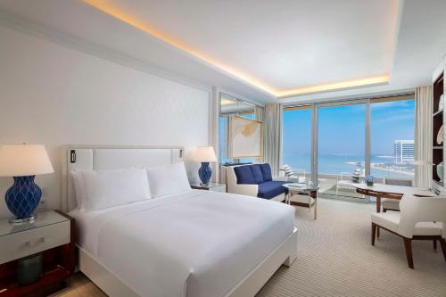 a white bedroom with a large bed and a view of the ocean at Waldorf Astoria Doha Lusail in Doha