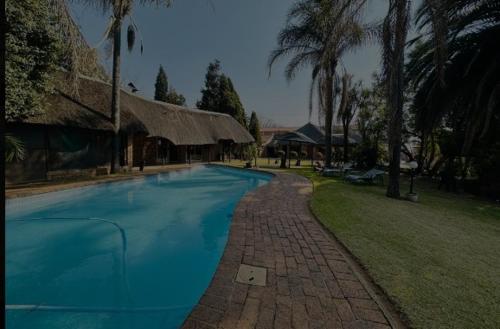 a blue swimming pool with a building and palm trees at Aero Airport Lodge in Kempton Park