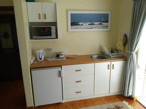 a kitchen with white cabinets and a sink and a microwave at Oppikrom Rivertide 36 in St Francis Bay