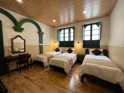 a room with three beds and a mirror at Hotel La Gran Casona in Tunja