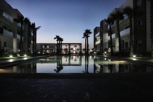 a large pool of water in a courtyard with palm trees at Appartement Casablanca in Dar Bouazza