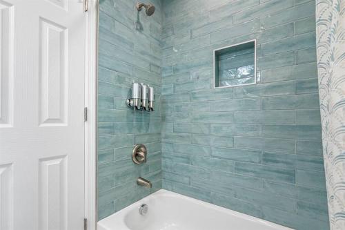 a bathroom with a tub and a shower with blue tiles at Downtown Dunedin Gem, Fully Renovated #2 in Dunedin
