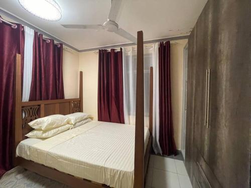 Ce lit se trouve dans un dortoir doté de rideaux rouges. dans l'établissement The Tropics Apartment Mombasa, à Mombasa