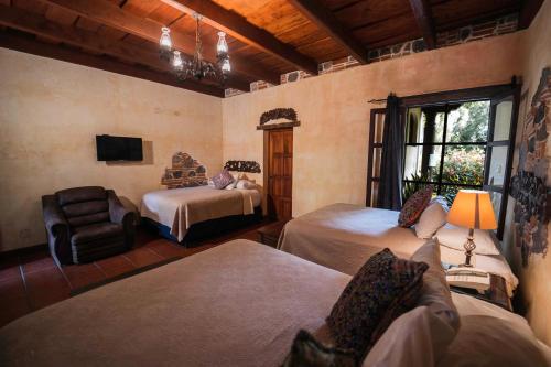 a bedroom with two beds and a chair and a window at Hotel Real Plaza in Antigua Guatemala