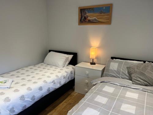 a bedroom with two beds and a lamp on a night stand at MJ Serviced Apartment up to 6 Guest - Luxurious living in West London next to Tube station & Central London in Hanwell