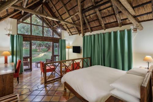 1 dormitorio con cama, cortinas verdes y mesa en Protea Hotel by Marriott Lusaka Safari Lodge, en Chisamba