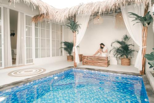 a woman sitting on a bench next to a swimming pool at Demoska Villa Jogja With Privatepool in Kejayan