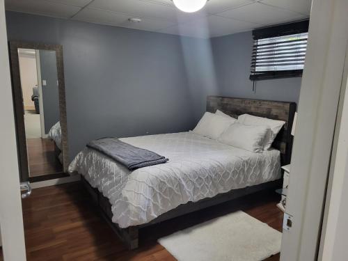 1 dormitorio con 1 cama con sábanas blancas y espejo en Private basement apartment en Saskatoon