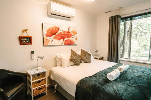 ein Schlafzimmer mit einem Bett, einem Stuhl und einem Fenster in der Unterkunft Alpine Riverside Cottages in Porepunkah