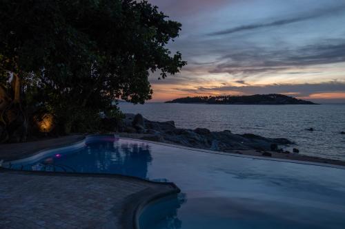 a swimming pool next to the ocean at sunset at Ampersand Resort in Bophut 