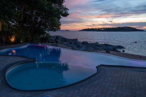 a swimming pool next to the ocean at sunset at Ampersand Resort in Bophut 