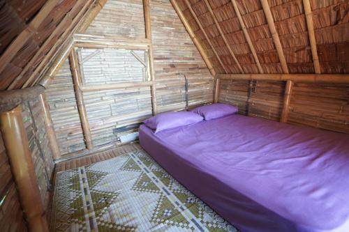 una camera da letto in una cabina di legno con un letto viola di Redang Campstay Bamboo House a Redang Island