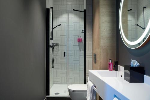 ein Bad mit einer Dusche, einem WC und einem Waschbecken in der Unterkunft Moxy The Hague in Den Haag