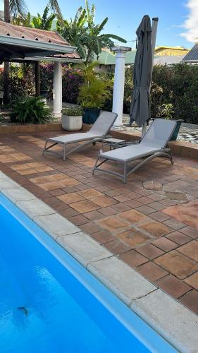 two lounge chairs and an umbrella next to a pool at Villa Osiris in Flic-en-Flac