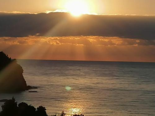 a sunset over the ocean with the sun peeking through the clouds at Spectacular villa near the beach! in Agia Paraskevi
