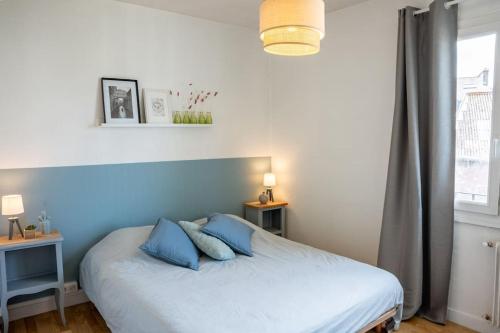 a bed with blue pillows in a bedroom with a window at Les Hirondelles By Nid'Ouest in Quimper