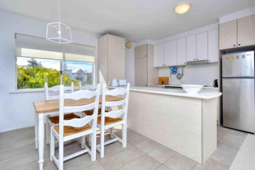 a kitchen with white cabinets and a table and a refrigerator at Beautiful, modern apartment seconds from beach in Perth
