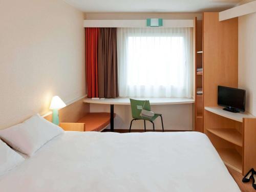 a hotel room with a bed and a desk and a window at ibis München City Nord in Munich