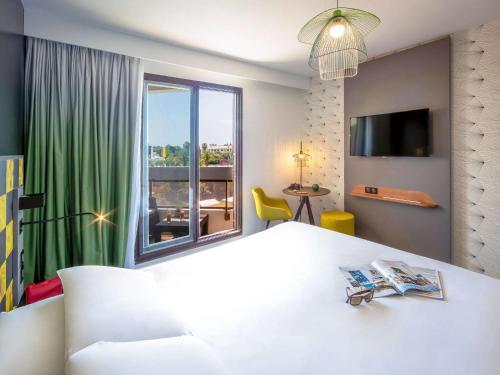 ein Schlafzimmer mit einem großen weißen Bett und einem großen Fenster in der Unterkunft Mercure Hyères Centre Côte d'Azur in Hyères