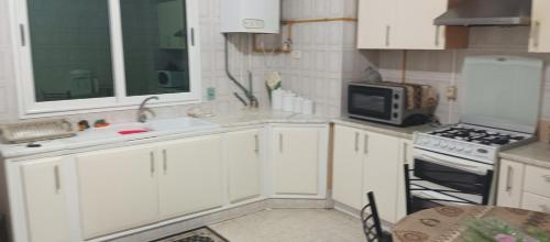 een keuken met witte kasten, een wastafel en een magnetron bij Well furnished appartment , Sahloul sousse in Sousse