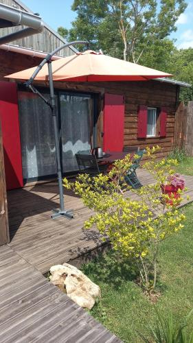 a house with a deck with an umbrella at La cabane au fond du jardin in Le Massegros