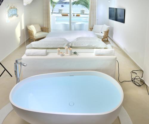 two beds in a room with a tub and a sink at Nissaki Boutique Hotel in Platis Yialos Mykonos