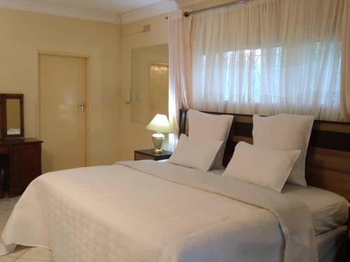 a bedroom with a large white bed with a window at Charming 6-Bed House with Swimming Pool in Harare in Harare