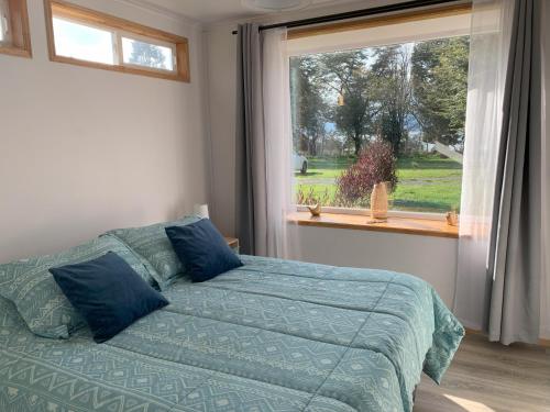 a bedroom with a bed with blue pillows and a window at Cabaña Familiar de Descanso y Paseo - Puyehue in Puyehue