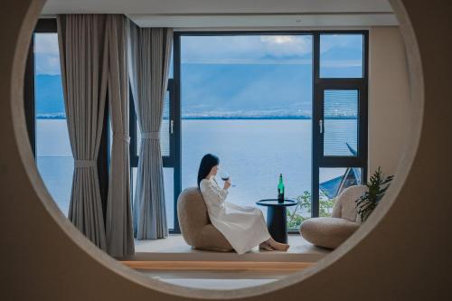 a woman sitting on a chair in front of a window at Dali Oriental Seaview Hotel -Dali Erhai in Dali