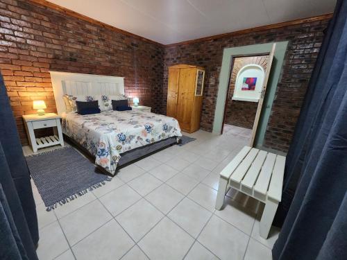 a bedroom with a bed and a bench and a brick wall at Flamboyant Guesthouse in Bela-Bela
