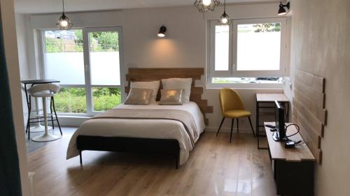 a bedroom with a bed and a desk and two windows at Studio 35m2 in Fougères