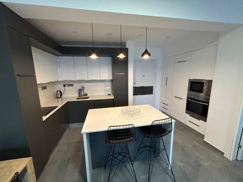 a kitchen with white cabinets and a island with two bar stools at Apartment Long Beach in Saint Yeorgios