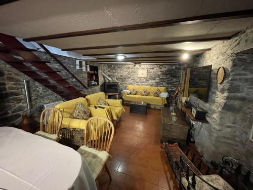 a living room with yellow furniture and a stone wall at CASA DOS FALCÕES casa rural de construção tradicional in Fajã da Ovelha