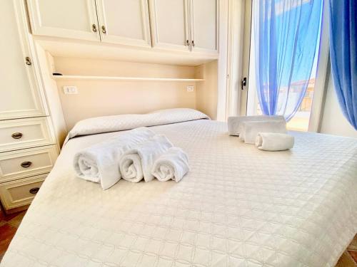 Una cama blanca con tres toallas enrolladas. en Casagliana Apartments, en Golfo Aranci